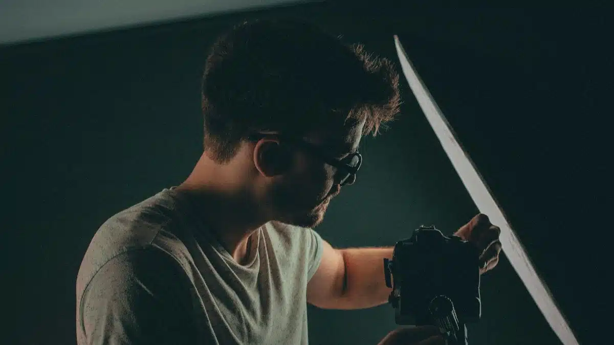 Photographer adjusting camera and equipment in a studio setting. Low light atmosphere.