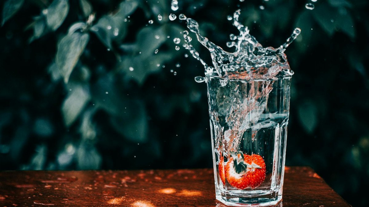 A vibrant strawberry splashes into a glass of water, captured mid-motion.