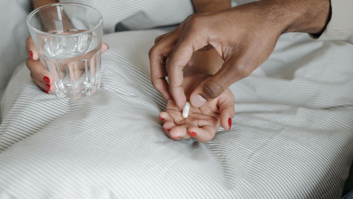 Close-up of hands offering a pill with a glass of water, symbolizing care and medication.