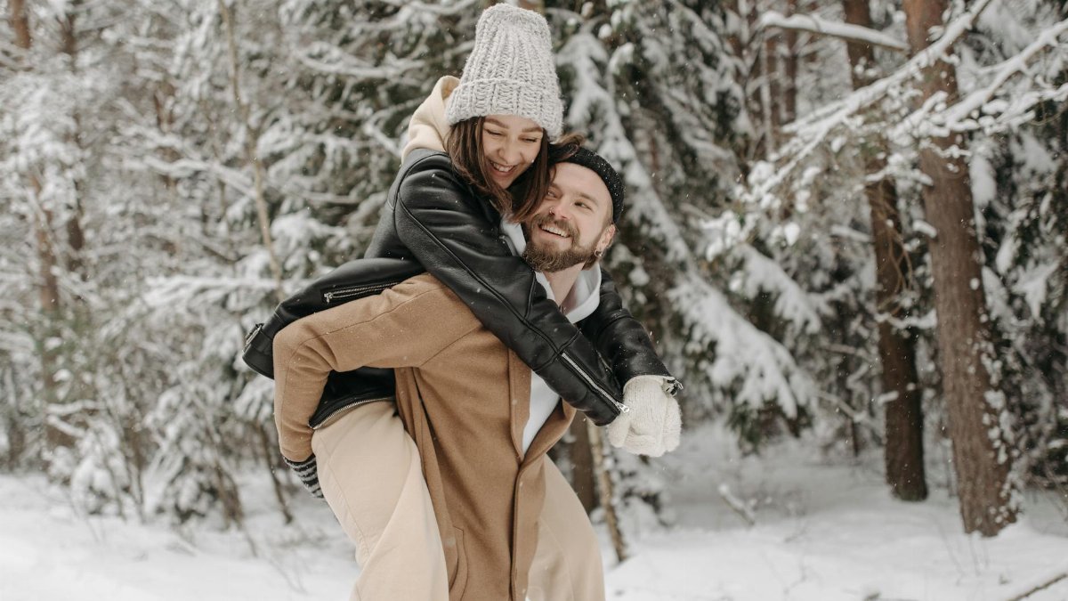 Joyful couple having fun in a snowy forest during winter, showcasing love and happiness.
