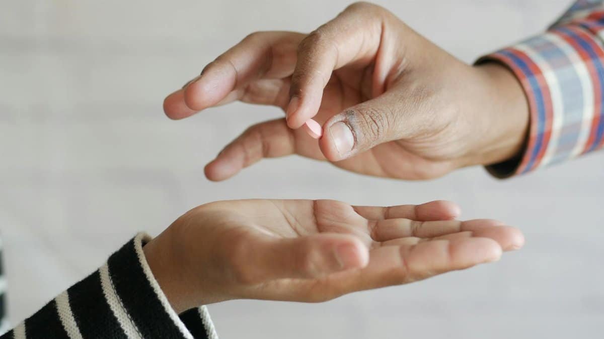 Close-up of hands exchanging a single pill, symbolizing medication sharing.