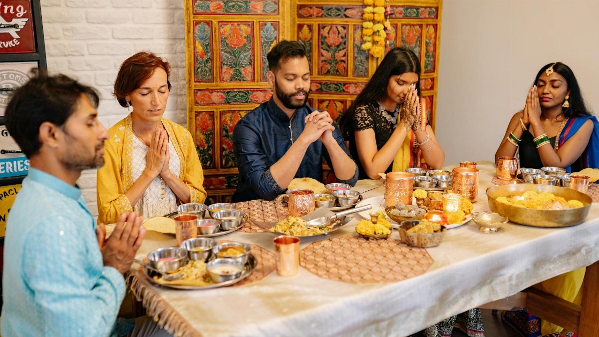 A family around a dinner table praying together during Diwali celebration, indoors.