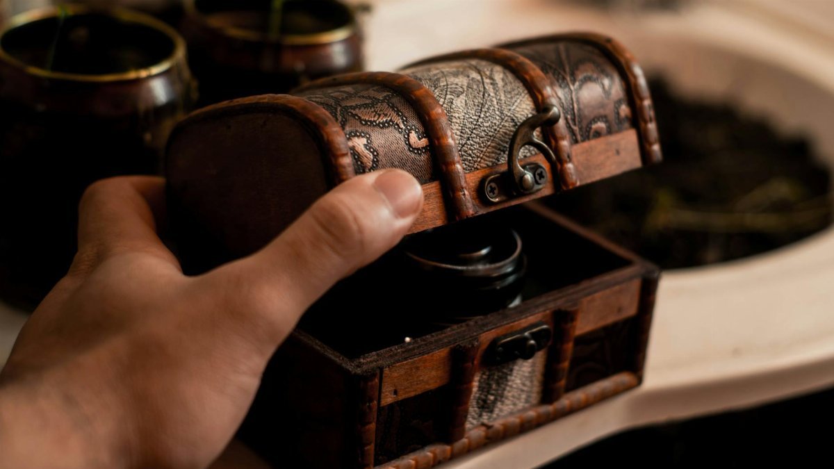 Crop anonymous male artisan opening small antique wooden chest placed on table at home