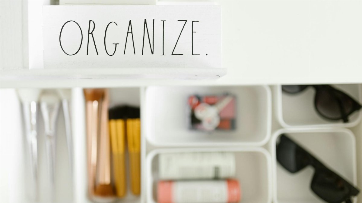 Stylish arrangement of makeup brushes, sunglasses, and accessories in white compartments with 'Organize' label.