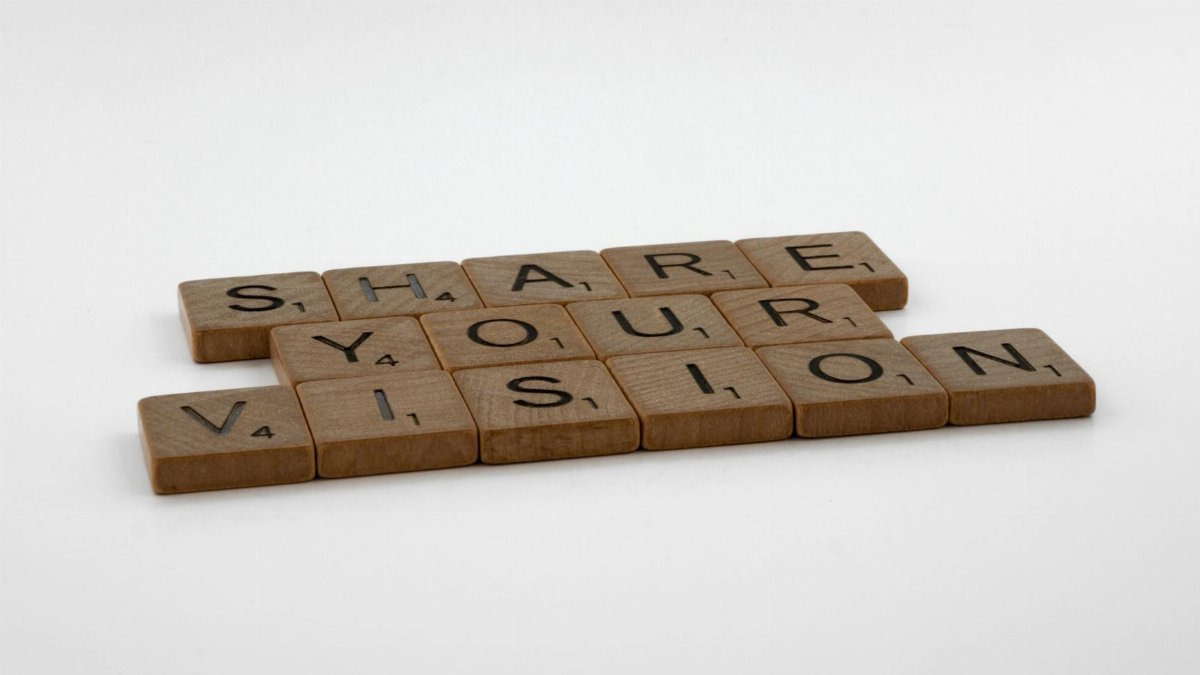 Wooden tiles spell 'Share Your Vision' on a white background, promoting creativity.