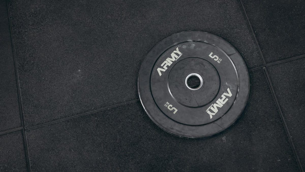A black 5 kg Army weight plate on a gym floor, ready for strength training.