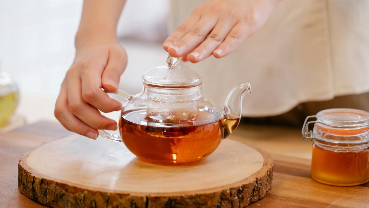 A close-up view of hands preparing herbal tea in a glass kettle. Warm and inviting.