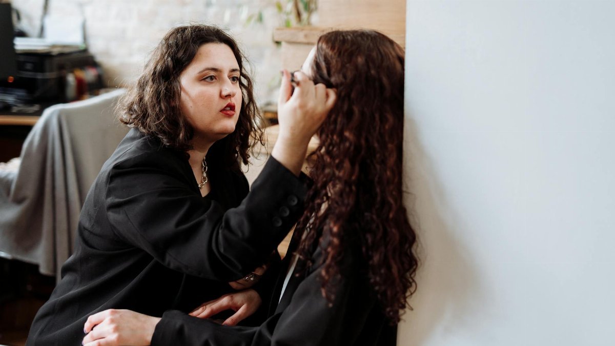 A heartfelt moment of friendship captured as one woman applies makeup to another indoors.