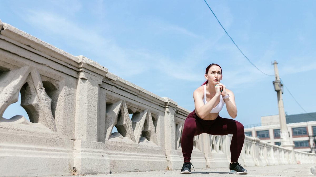 Woman performing a squat exercise outdoors beside a concrete railing under a clear sky.