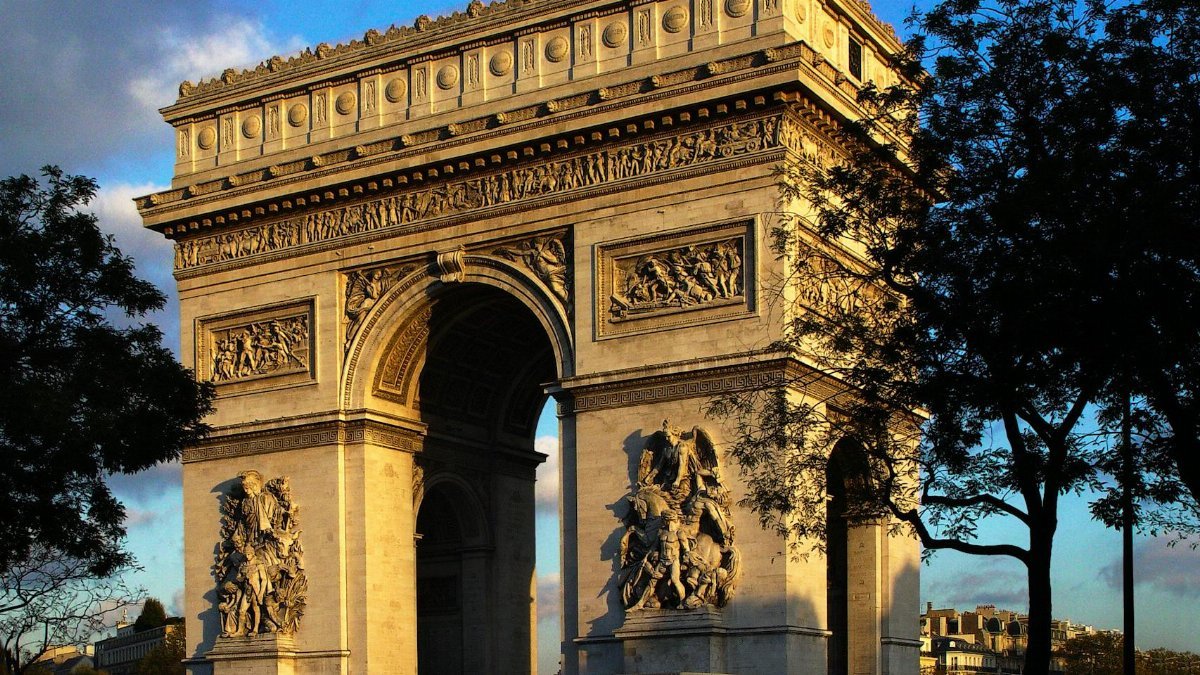 The iconic Arc de Triomphe illuminated by the warm glow of sunset in the heart of Paris, France.