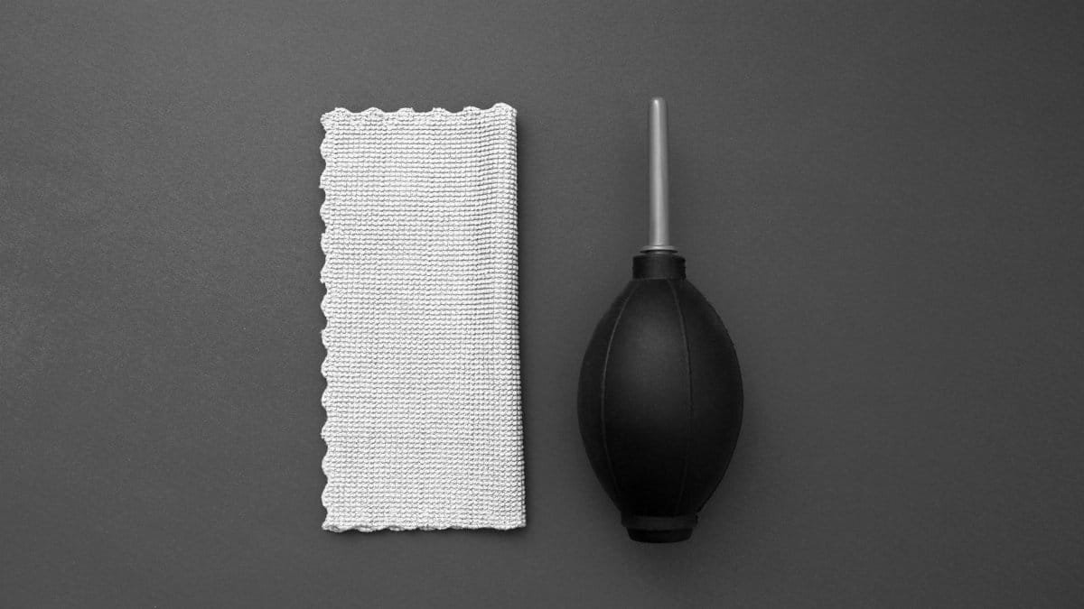 Overhead view of a camera cleaning blower and microfiber cloth on a gray background.