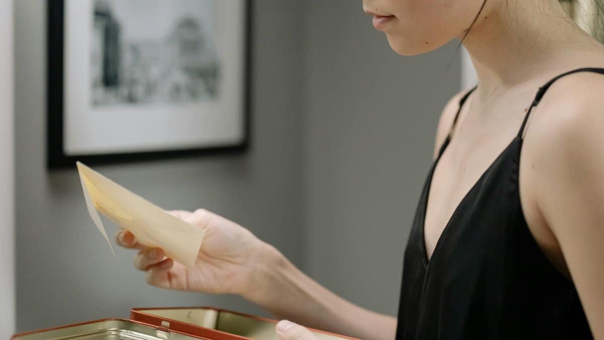 A woman in a black dress holds a photograph from an open keepsake box indoors.