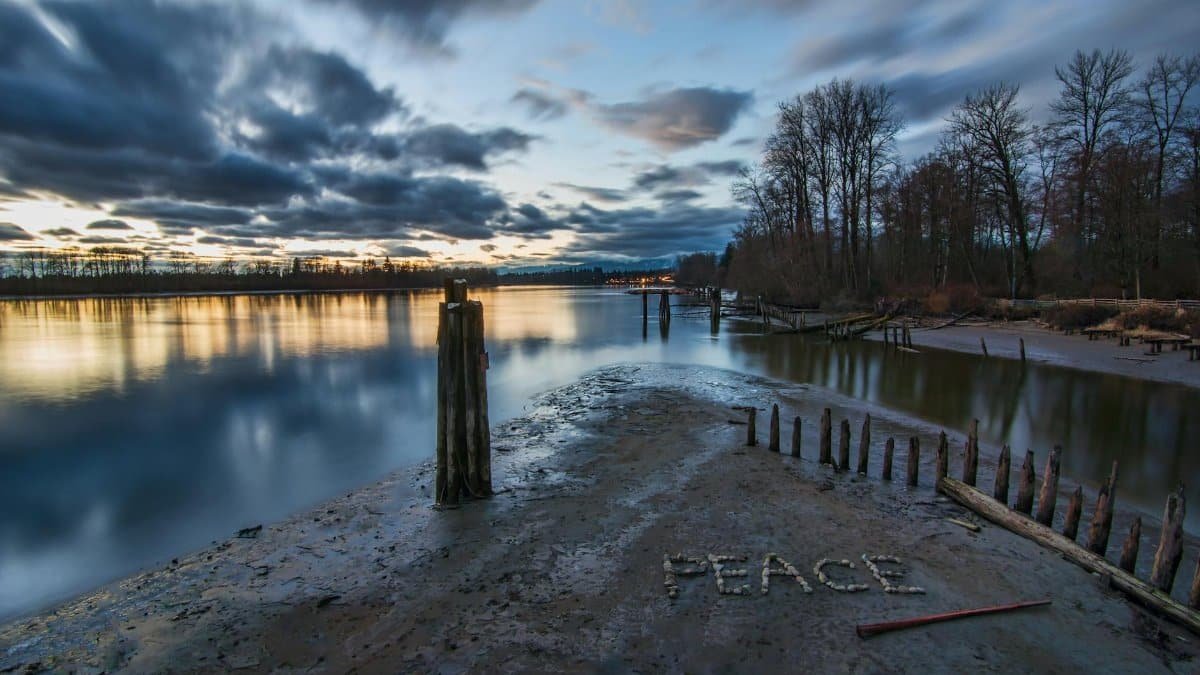Peaceful riverbank scene during twilight in Maple Ridge, Canada, with 'PEACE' written in sand.