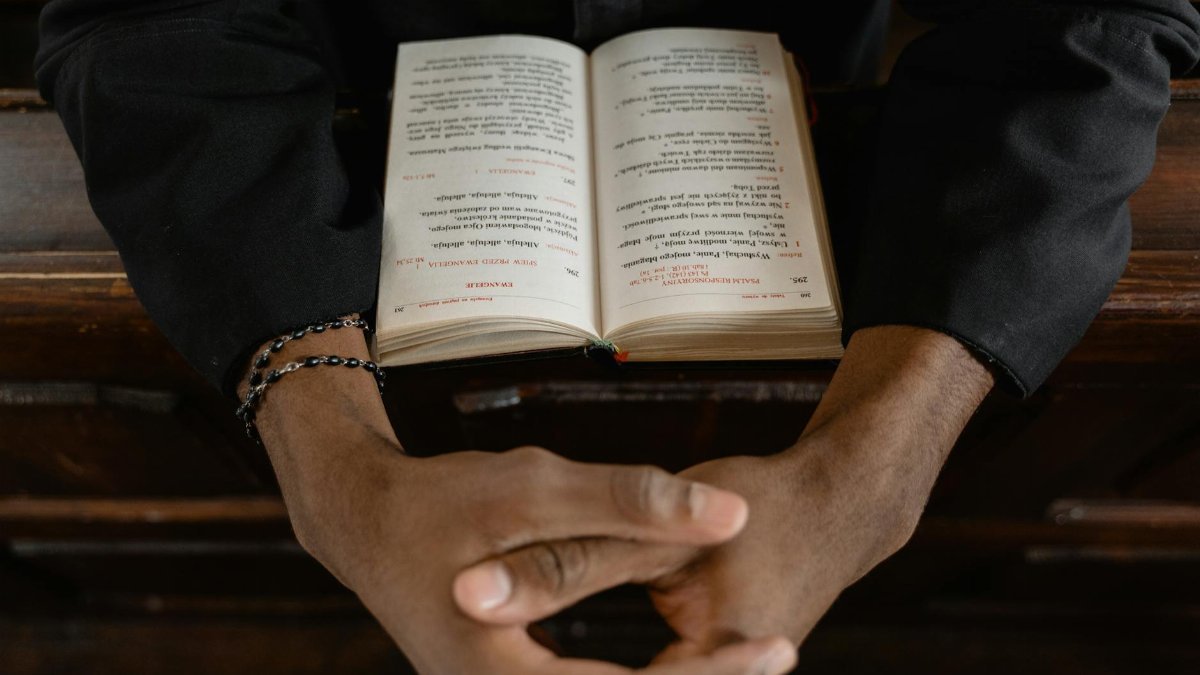 Close-up of hands clasped over an open Bible, symbolizing prayer and faith.