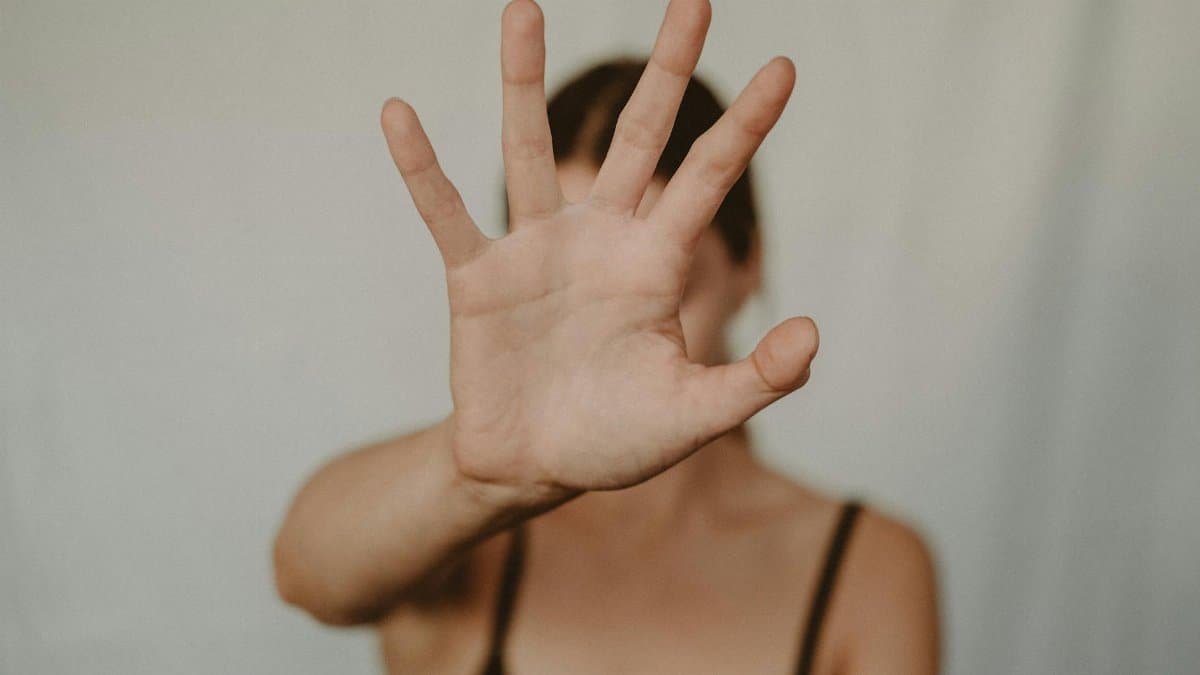 A woman's hand extended forward in a stop gesture, with a soft blurred background.