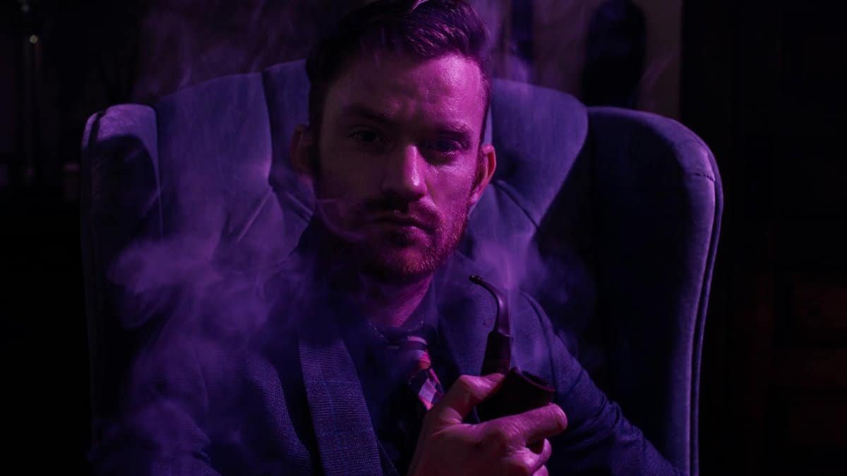Stylish man in a dark setting, smoking a pipe, exuding confidence and mystery.