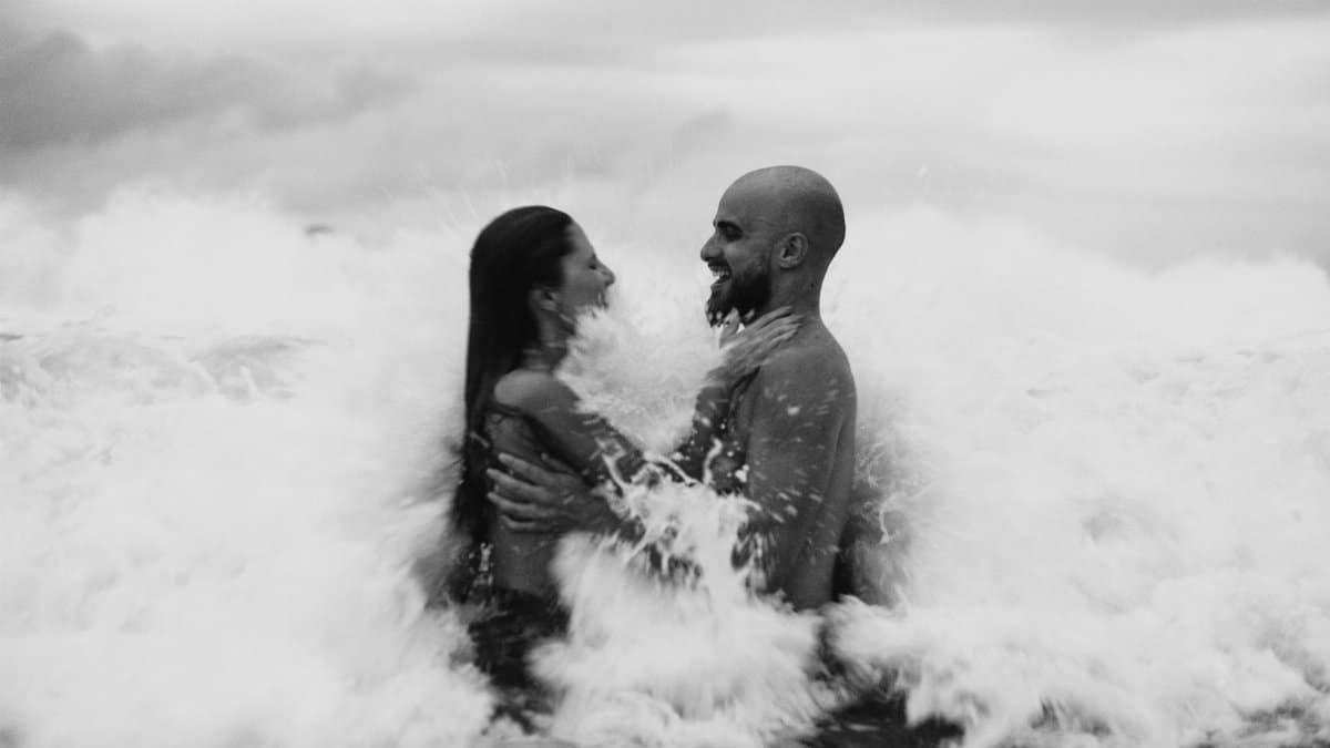 A couple embracing in the ocean waves, captured in black and white, exuding love and joy.