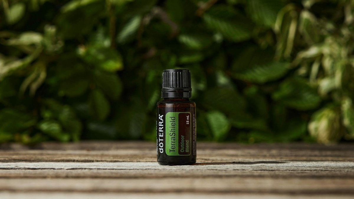 A small bottle of TerraShield essential oil placed on a wooden surface with a lush greenery background.