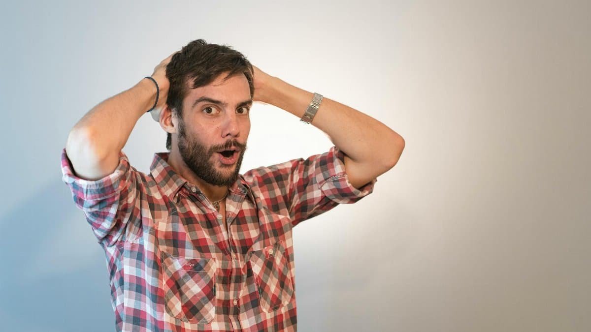 A surprised man with a beard, holding his head in astonishment in a studio setting.