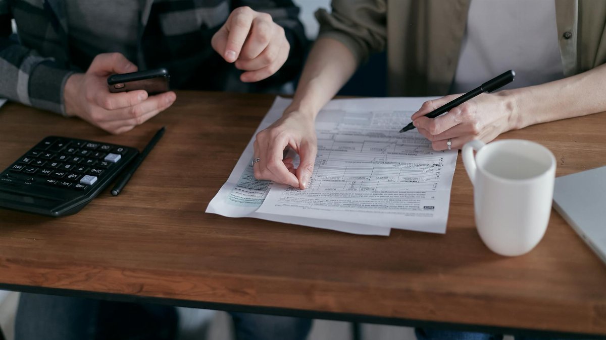 Couple managing finances at home with a calculator, smartphone, and documents.