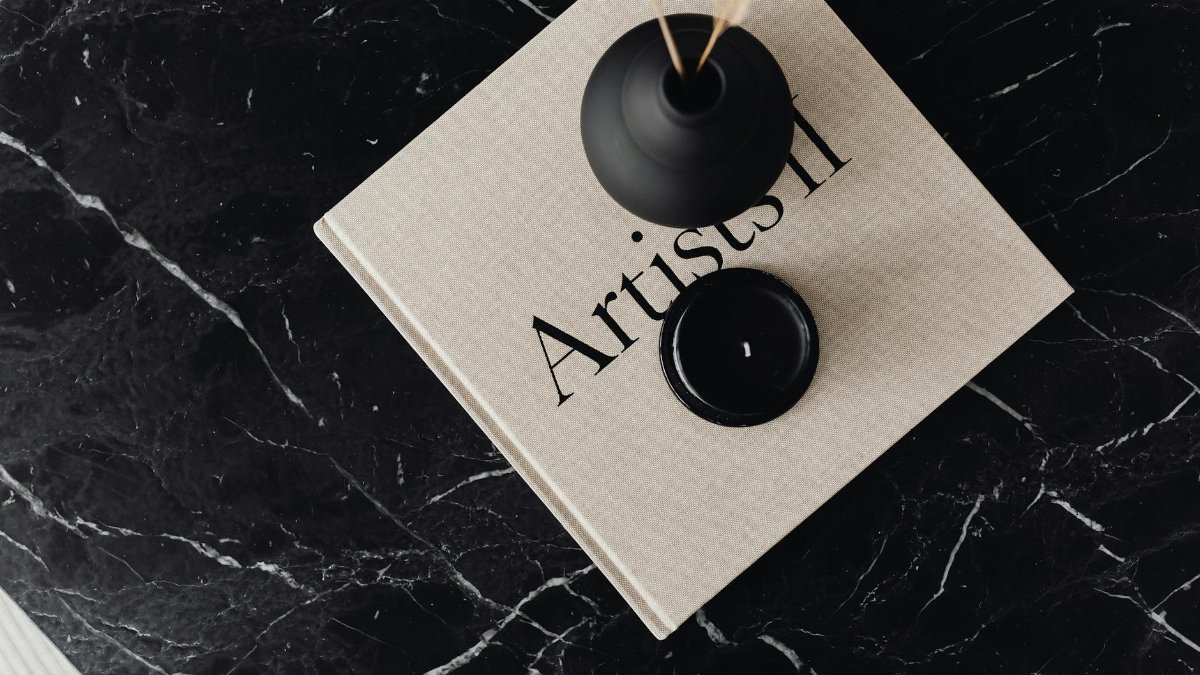 Top view of minimalist decor with a vase and book on a black marble table surface.