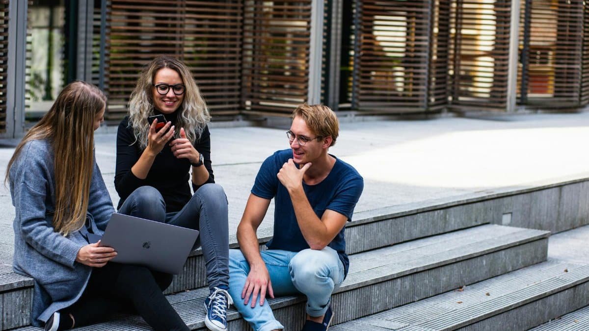 Three young professionals having a friendly chat while sitting on outdoor steps.