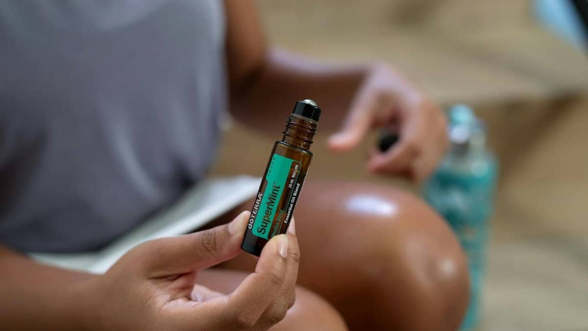 A woman holding a roller bottle of doTERRA SuperMint essential oil close-up shot.