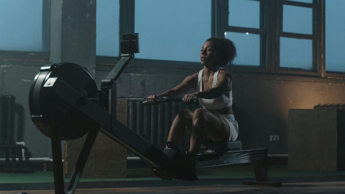 A woman working out on a rowing machine indoors, showcasing strength and focus.