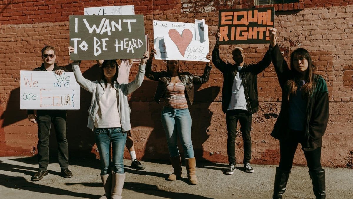 Diverse group holding protest signs for equality and peace near a brick wall.