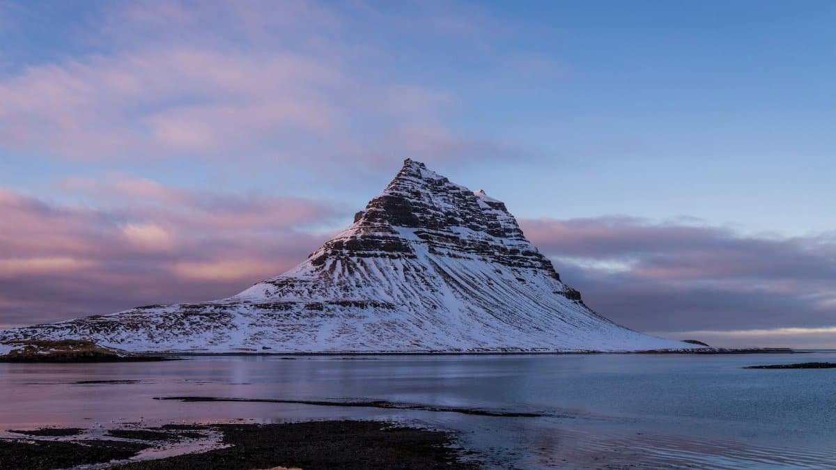 Stunning view of snow-covered Mount Kirkjufell in Iceland during dusk, reflecting on tranquil waters.