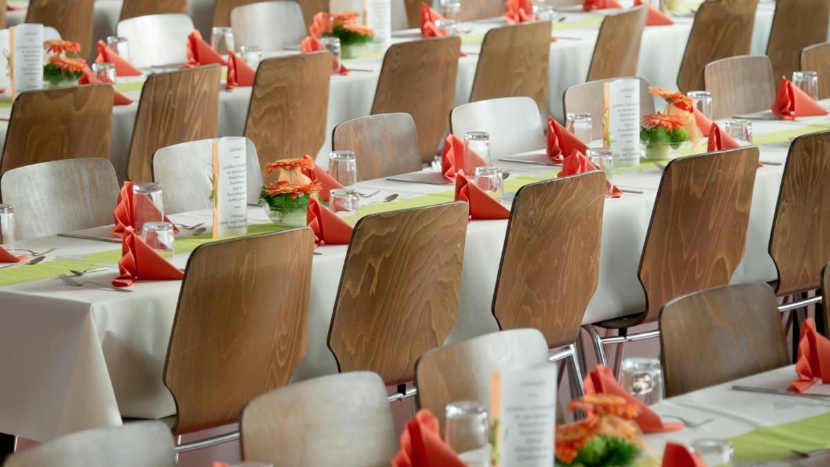 Beautifully arranged tables with wooden chairs for a formal event, adorned with orange flowers.