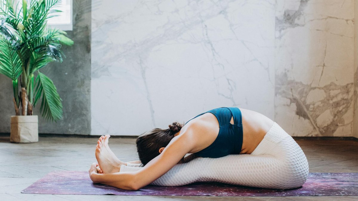 Woman performing a seated forward bend yoga pose on a mat indoors.