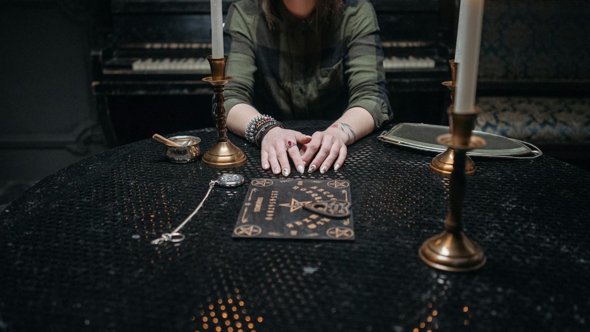 Woman sitting at a table with candles and a Ouija board, ambient setting.