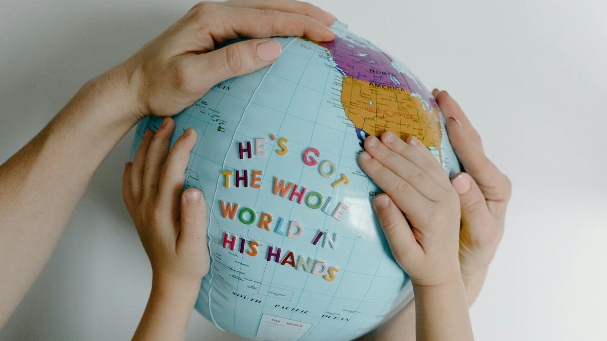 Hands of different ages holding a globe with the text 'He's got the whole world in His hands.'