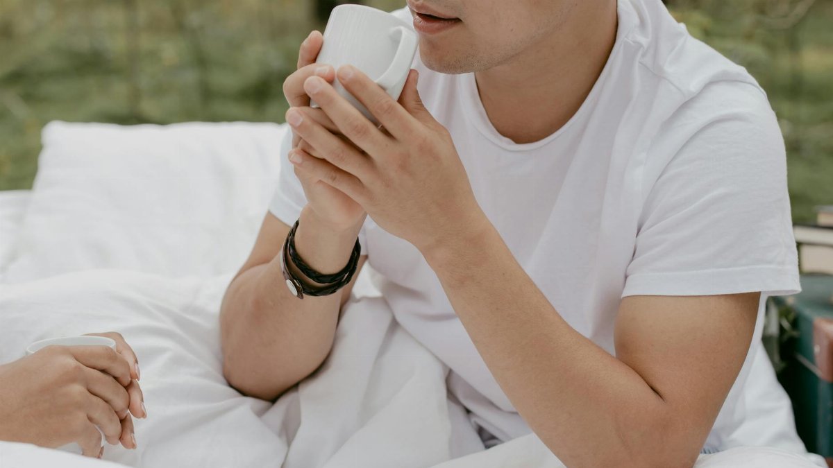 Man enjoying a cup of coffee outdoors, wrapped in a blanket, exuding a relaxed morning vibe.