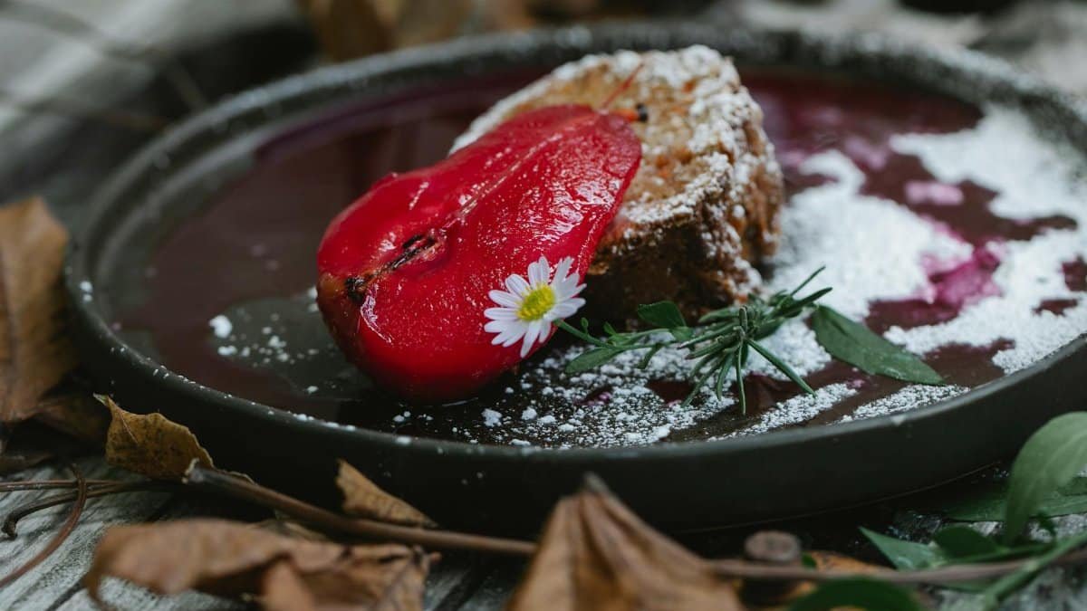 Appetizing composition of yummy sweet pie slice garnished with red pear and chamomile while served on black plate