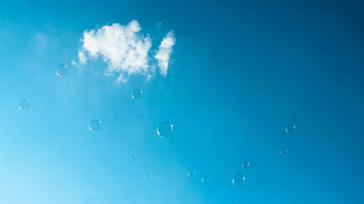 Ethereal bubbles drift against a backdrop of a bright blue sky with soft clouds.