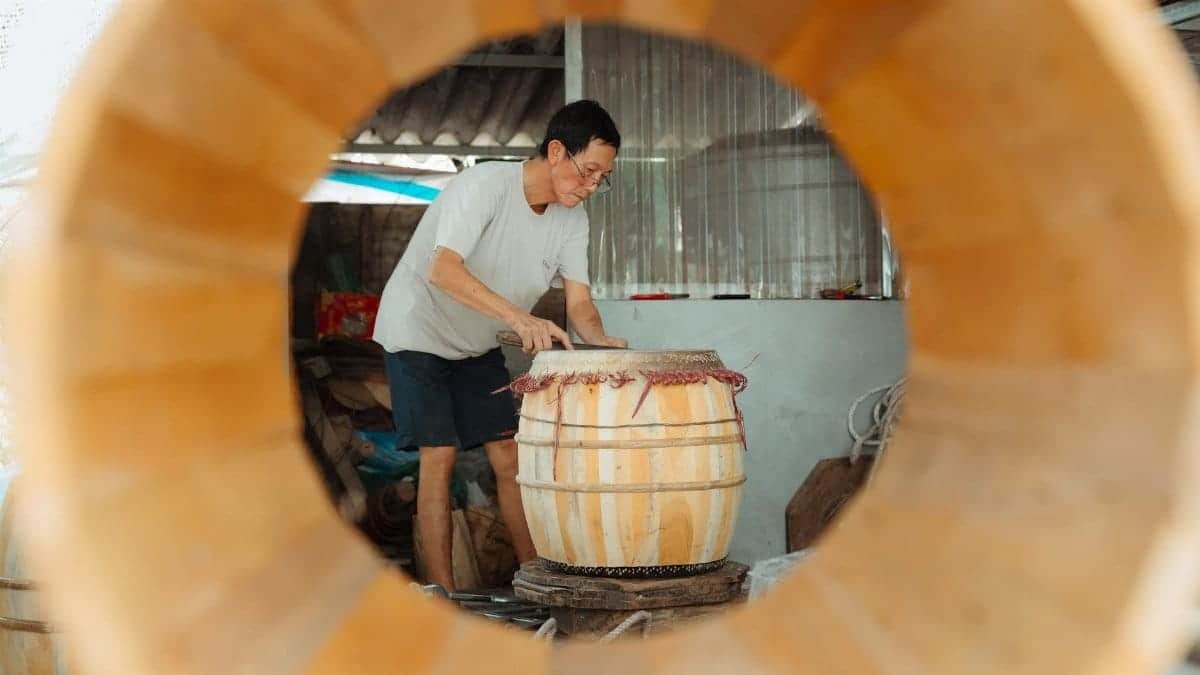 Skilled artisan works on a wooden drum in a workshop. Focus on craftsmanship and tradition.
