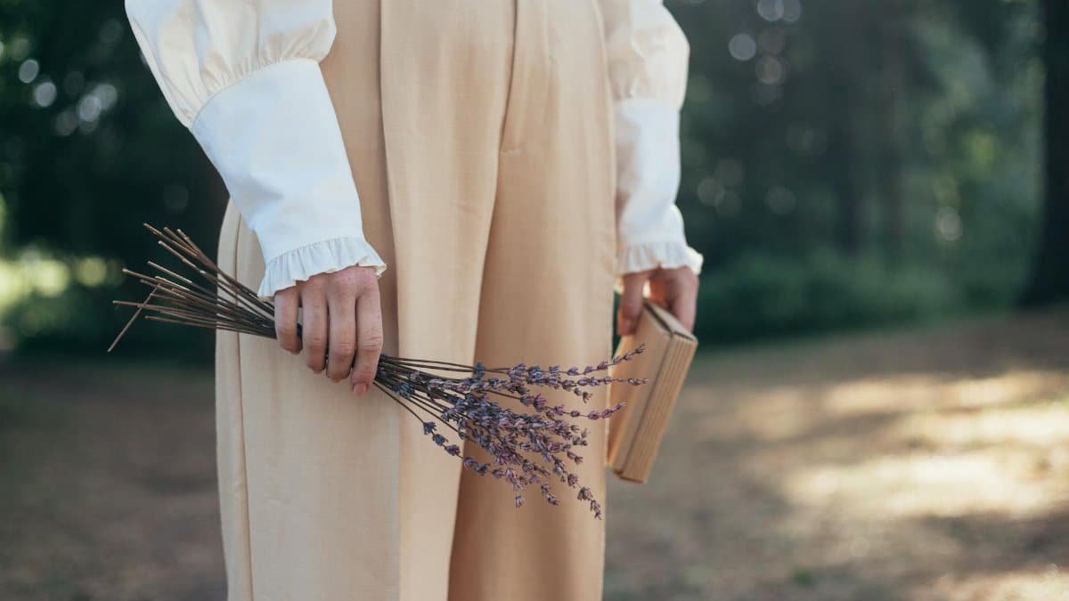 A woman standing outdoors holding a lavender bouquet, evoking nostalgia.