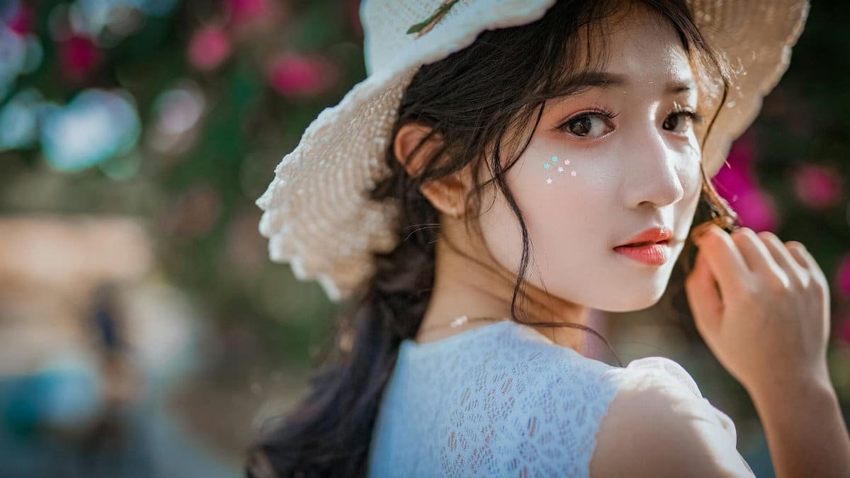 Portrait of a young Asian woman wearing a sun hat, surrounded by vibrant flowers.