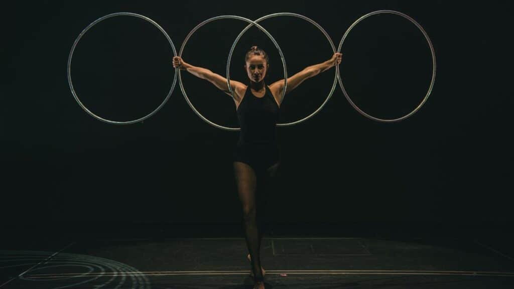 A skilled gymnast performs with hoops on stage, showcasing grace and control in a dramatic setting.