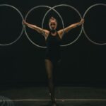 A skilled gymnast performs with hoops on stage, showcasing grace and control in a dramatic setting.