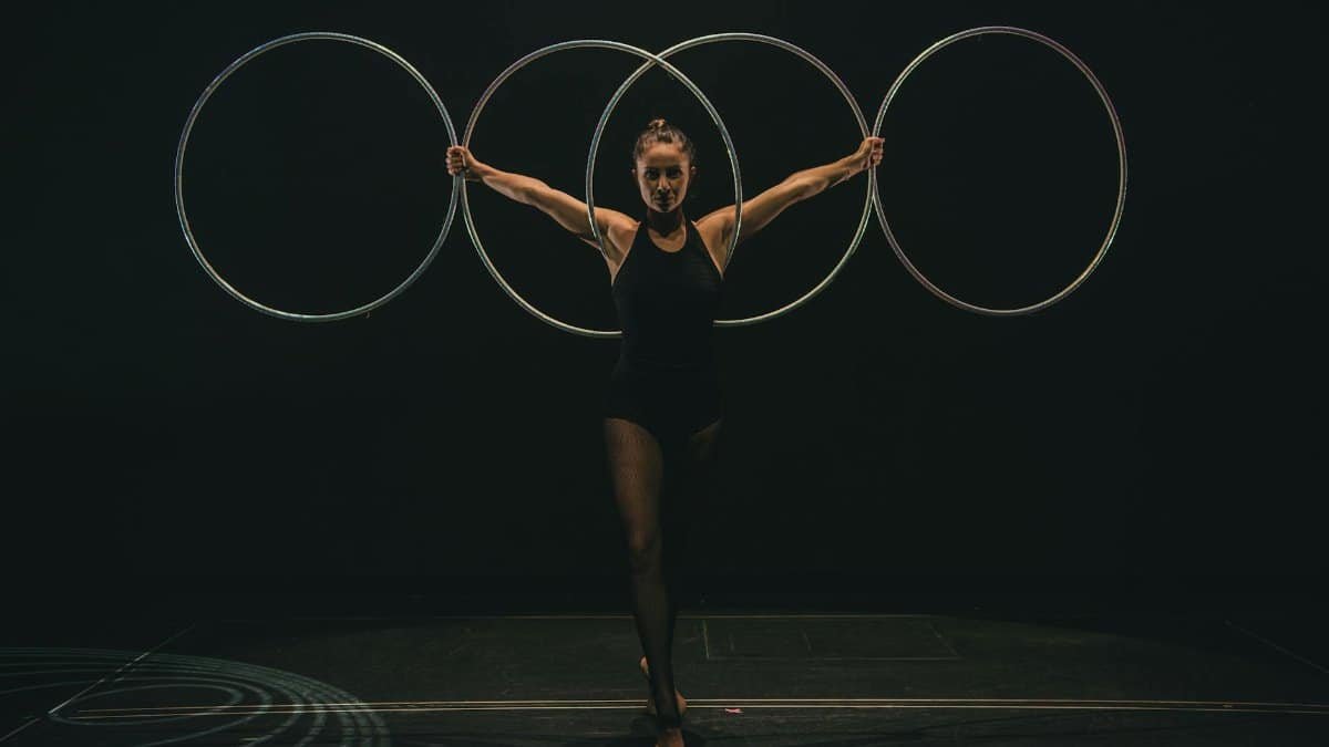 A skilled gymnast performs with hoops on stage, showcasing grace and control in a dramatic setting.