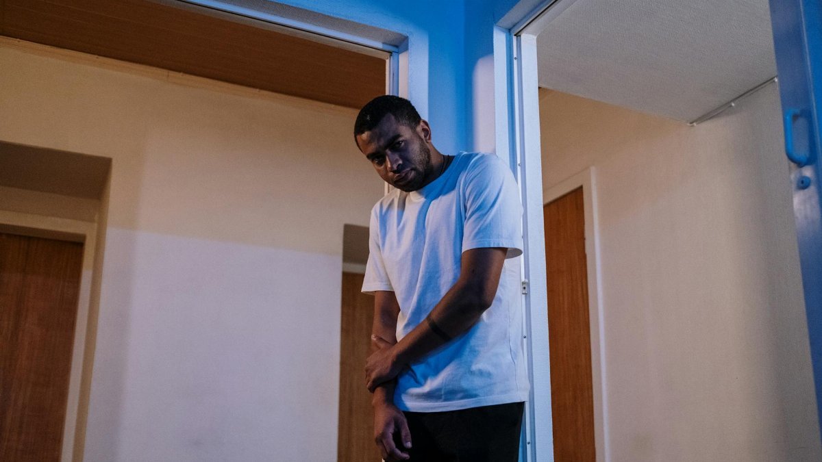 Thoughtful man standing alone in doorway with moody lighting and minimalistic decor.