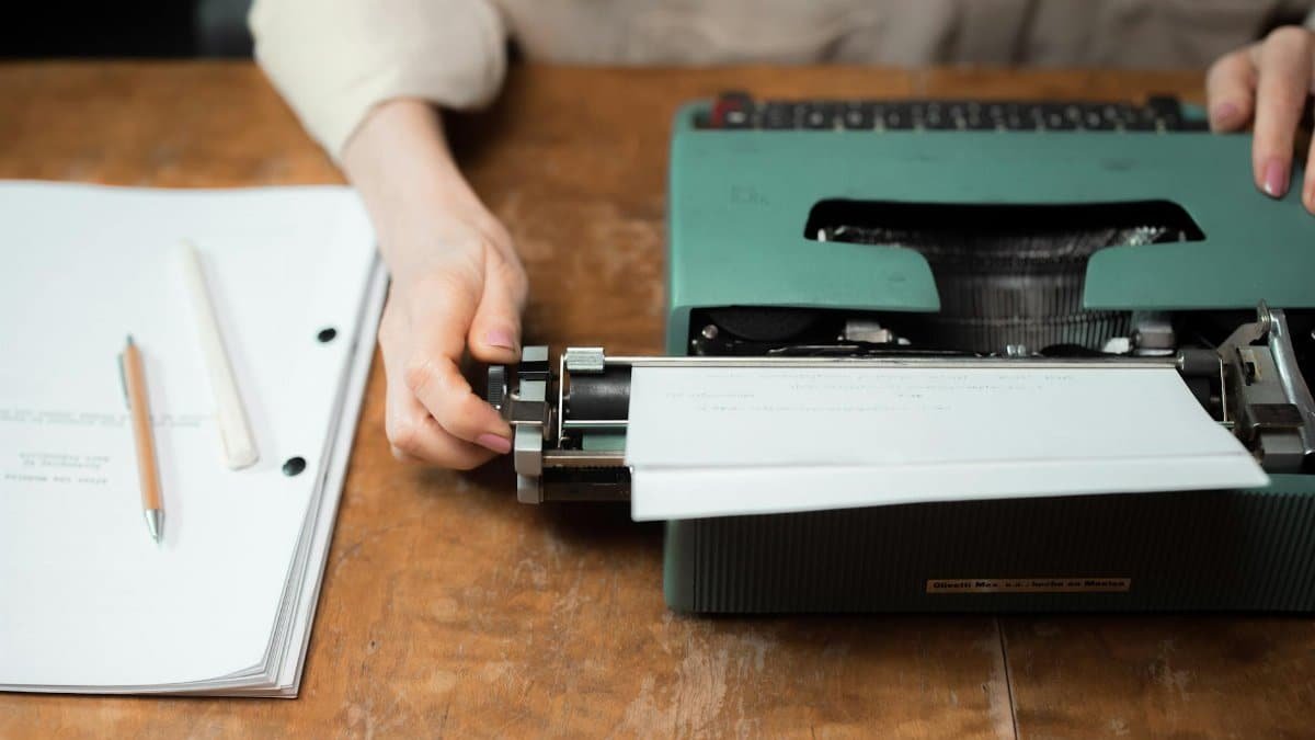 Close-up of hands typing on a vintage green typewriter with papers on a wooden desk.