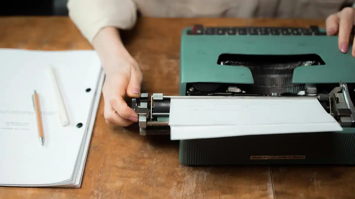 Close-up of hands typing on a vintage green typewriter with papers on a wooden desk.