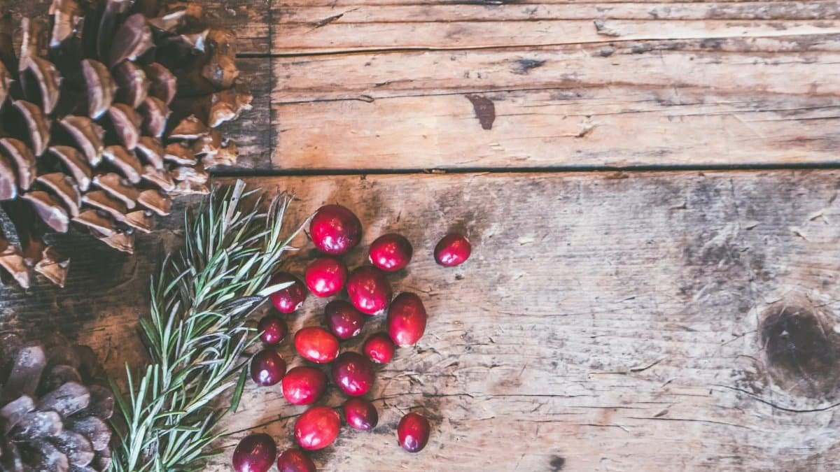 Top view of rustic holiday decor featuring pinecones, cranberries, and rosemary on a wooden surface.