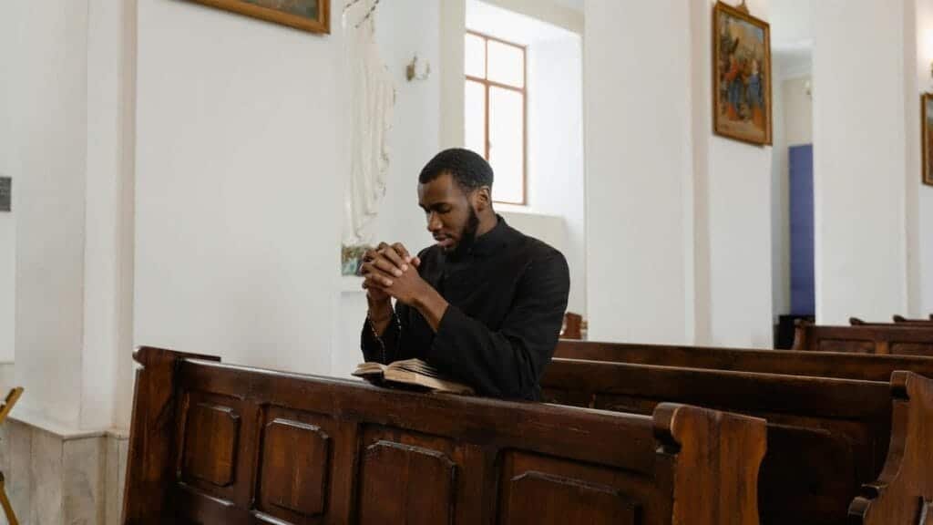 African American priest in deep prayer at a serene church setting.