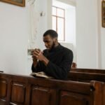 African American priest in deep prayer at a serene church setting.
