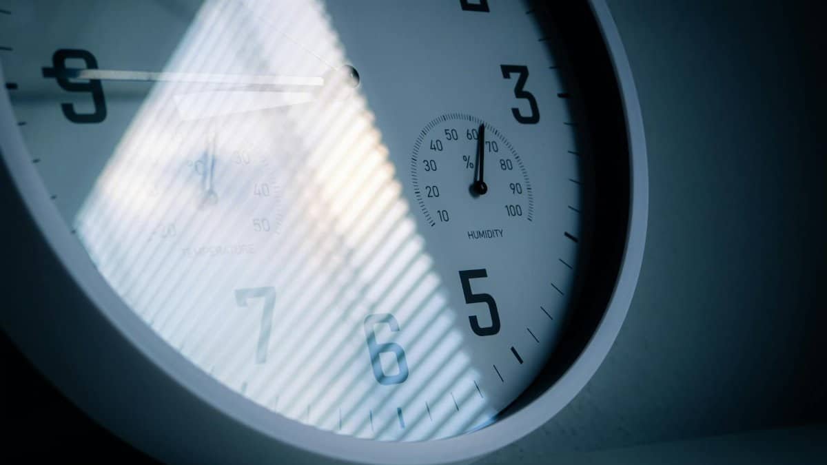 A close-up of a wall clock showing time and humidity, reflecting light and shadows.